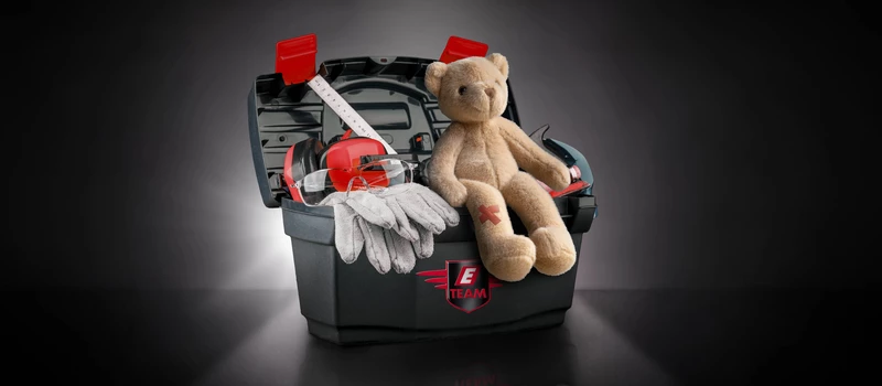 Werkzeugkiste mit Handschuhen, Schutzbrille und Teddybär mit Pflaster.