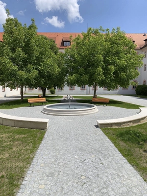 Weg mit Sitzplätzen am gefüllten Brunnen